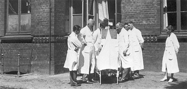 Ärztinnen - geduldete Außenseiterinnen Vorsichtiger Blick aus der Distanz, die Herren Ärzte diskutieren das weitereVorgehen bei einem Patienten, UKE, 1926.