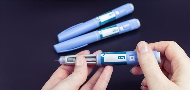 Drei Semaglutid-Stifte liegen auf einem Stift. Eine Person hat bei einem der Stifte den Deckel angenommen.