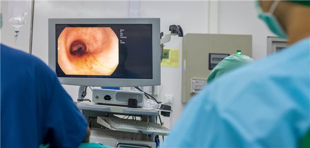 Ein Arzt in einem hellblauen Schutzkittel führt eine Koloskopie im Operationssaal eines Krankenhauses durch.