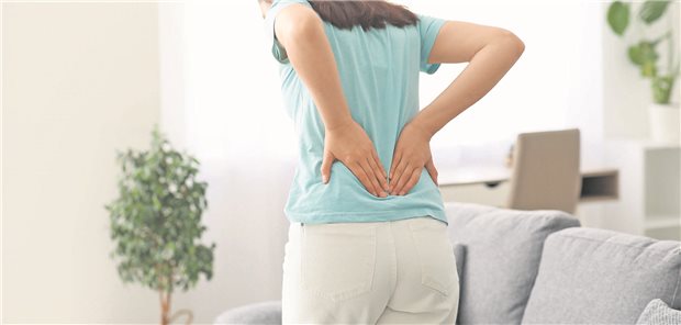 Eine junge Frau hält sich bei Rückenschmerzen beide Hände an den unteren Rücken.