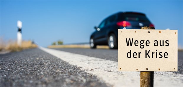 Fahrendes Auto, im Vordergrund ein Schild mit der Aufschrift "Wege aus der Krise"