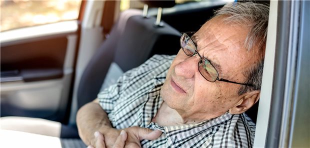 Ein Mann sitzt auf dem Fahrersitz seines Autos und hält sich beide Hände an die Brust.