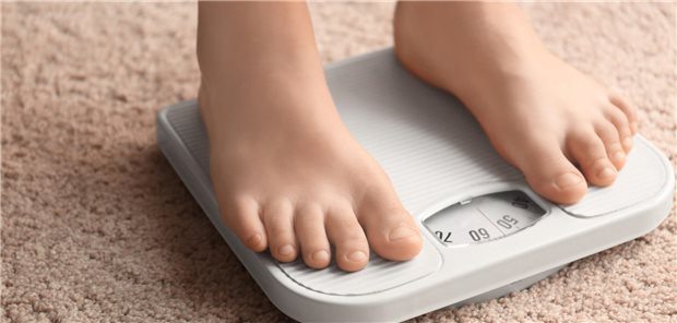 Übergewichtiges Kind steht zu Hause auf der Waage.