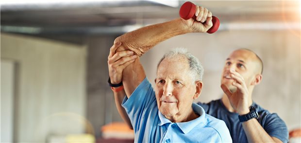 Ein älterer Herr bekommt von einem Trainer gezeigt, wie er eine Hantel benutzen soll. 
