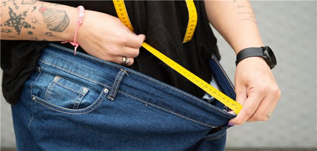 Mann misst Hosenumfang mit Massband.