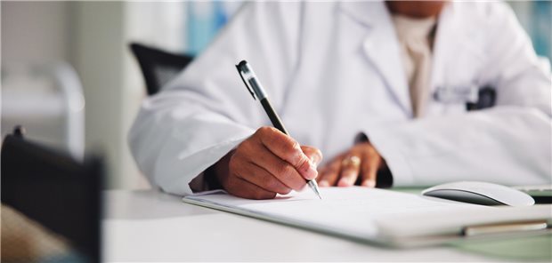 Ein Arzt sitzt am Schreibtisch in einer Klinik und erstellt einen medizinischen Befund für die Krankenakte eines Patienten.