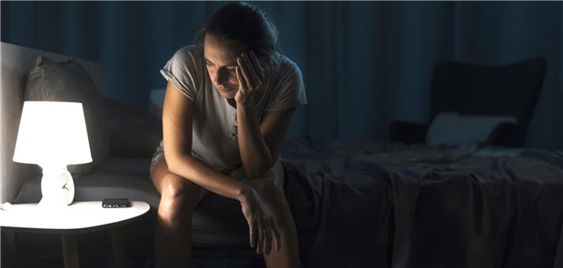 Frau sitzt nachts auf ihrem Bett und schaut ins Licht ihrer Nachttischlampe. 