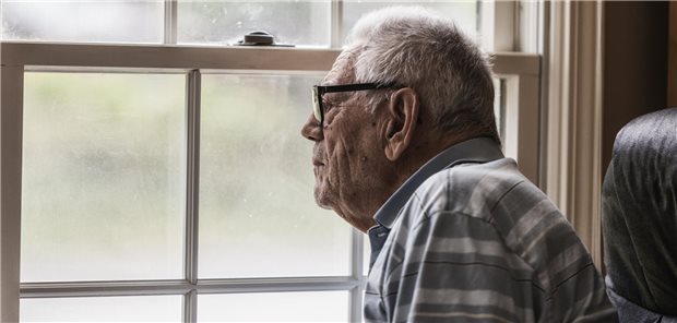 Älterer Mann sitzt am Fenster und blickt hinaus