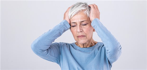 Eine ältere Frau, die sich mit schmerzverzerrtem Gesicht den Kopf hält, da sie unter Kopfschmerzen leidet.