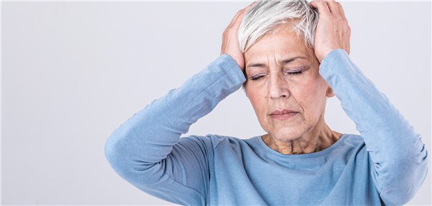 Eine ältere Frau, die sich mit schmerzverzerrtem Gesicht den Kopf hält, da sie unter Kopfschmerzen leidet. 
