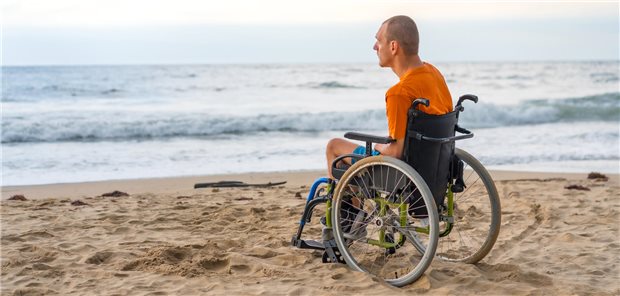 Ein junger Mann sitzt im Rollstuhl am Strand.