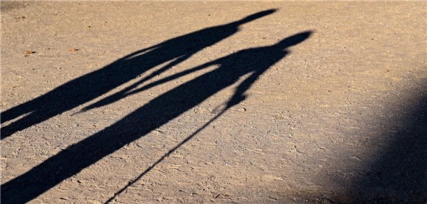 Schatten von zwei Personen, die Frau geht am Stock. 