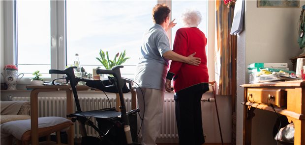 Pflegerin zeigt einer älteren Frau etwas an einem Fenster.