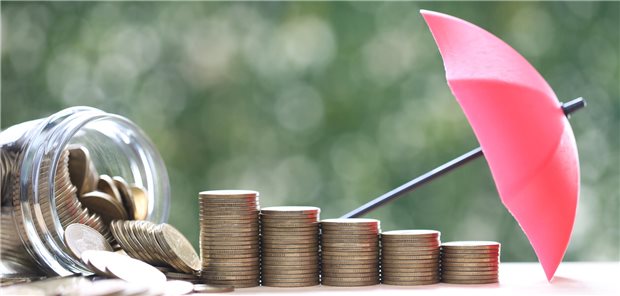 Geldmünzen zu Säulen gestapelt, davor ein Mini-Regenschirm, um Schutz vor Risiken zu symbolisieren. 