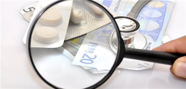 Eine Lupe nimmt Tablette und Geldschein ins Visier.