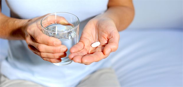 Patient hält Wasserglas in der einen Hand, in der anderen eine Tablette. 