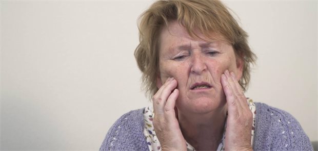 Eine ältere Frau fässt sich mit den Händen ins Gesicht