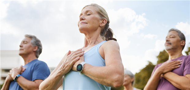 Eine Gruppe Menschen verschiedener Ethnien, die im Park Meditation praktizieren und dabei ihre Atmung trainieren.