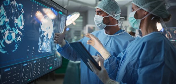 Eine Chirurgin und ein Chirurg beraten sich in einem schwach beleuchteten Operationssaal anhand des die Gehirnscans eines Patienten auf einem großen Bildschirm über das korrekte operative Vorgehen.