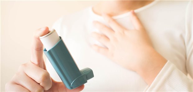 Ein junger Mensch hält einen Inhalator zwischen Daumen und Zeigefinger kurz vor der Inhalation.